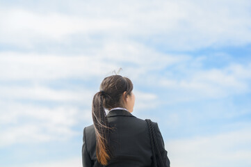 スーツ姿の新入社員の女性が青空を見上げる後ろ姿