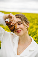 Enjoying a croissant in a vibrant yellow flower field on a sunny day