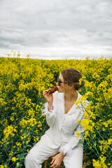 Young woman enjoys snack in rapeseed field under cloudy sky during late afternoon
