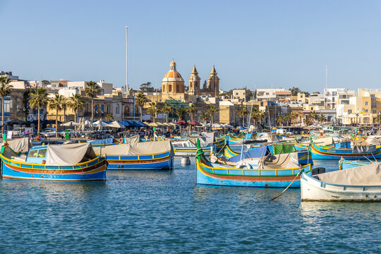 Malta, Marsaxlokk Harbor. Our Lady of Pompei church in background. Luzzijiet, plural of luzzu, colorful traditional Maltese fishing boats.