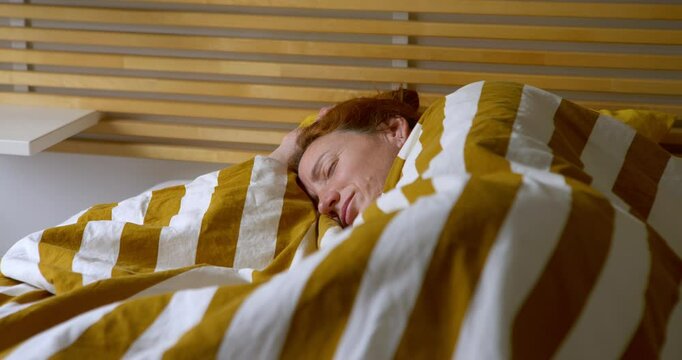 Adult woman sleeping in bed in her bedroom slowly opens her eyes. Close-up