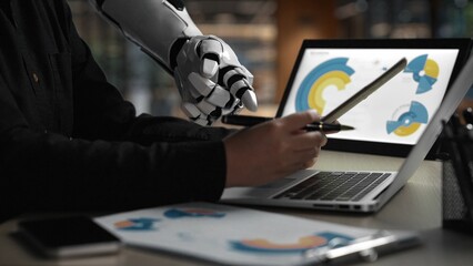 A sleek robotic arm collaborates with a human in a modern workspace, displaying digital graphs and...