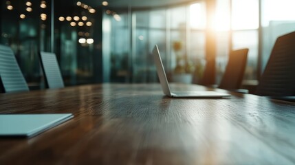 A contemporary conference room featuring a sleek wooden table, a single open laptop, and large glass windows allowing natural light to flood the space, creating a productive atmosphere.