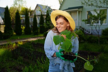 Portrait of a smiling gardener woman standing next to her green garden holding a young seedlings...