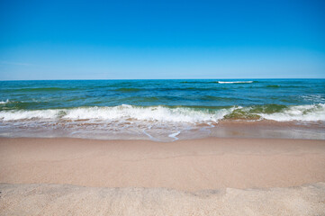 Empty, sandy beach and sea waves by summer sunny  day