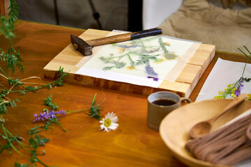 Creative DIY project with summer wildflowers: floral imprint technique using hammer on paper, top view of botanical art process on rustic wooden table