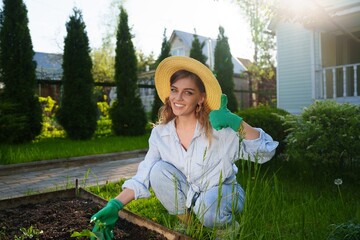 Portrait of a smiling gardener woman in the garden planting plants in the soil , dressed in a shirt...