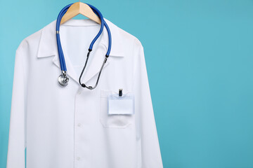 Doctor's coat with stethoscope and badge on hanger against blue background. Space for text