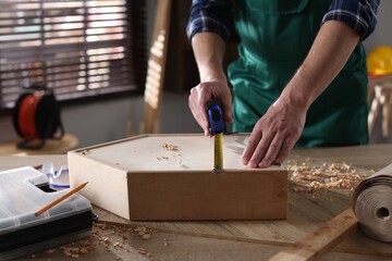 Man measuring wooden box with tape at table indoors, closeup