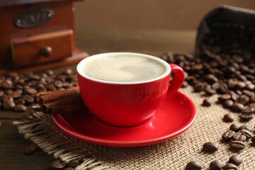 Aromatic coffee in cup, beans, cinnamon and grinder on wooden table, closeup