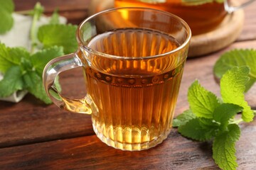 Aromatic lemon balm tea in glass cup and fresh leaves on wooden table, closeup