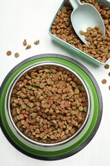Dry pet food in feeding bowl, container and scoop on light background, flat lay