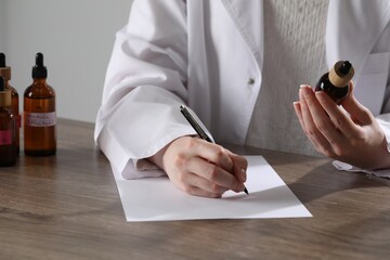Professional perfumer developing luxury perfume at wooden table in laboratory, closeup