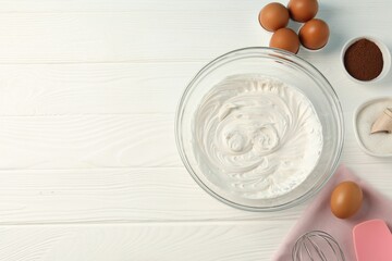 Bowl with whipped cream, whisk and ingredients on white wooden table, flat lay. Space for text
