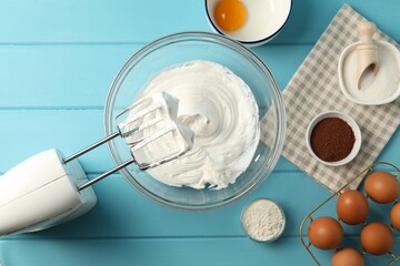 Bowl with whipped cream, hand mixer and ingredients on light blue wooden table, flat lay