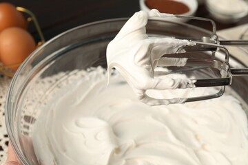 Hand mixer with whisks and bowl of whipped cream on table, closeup