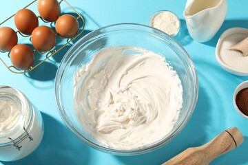 Whipped cream in bowl and other products on light blue table, above view