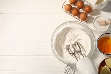 Hand mixer with whipped cream, eggs and other products on white wooden table, flat lay. Space for...