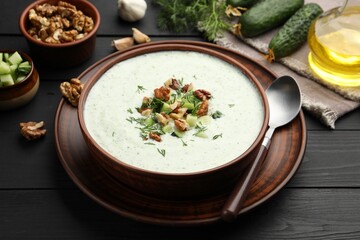 Tasty cucumber soup with dill and walnuts served on black wooden table, closeup