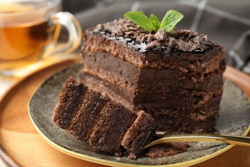 Piece of delicious chocolate cake with mint and tea on table, closeup