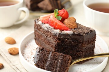 Piece of delicious chocolate cake with strawberry, almonds and tea on table, closeup