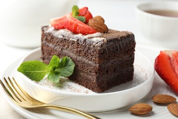 Piece of delicious chocolate cake with strawberry, almonds and mint on table, closeup