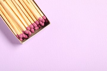 Matches in open box on violet background, top view. Space for text