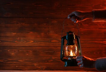 Woman holding vintage kerosene lantern near wooden wall, closeup. Space for text