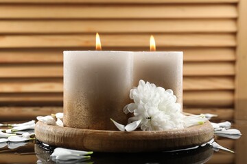 Burning candles and beautiful flowers on wet black mirror surface, closeup