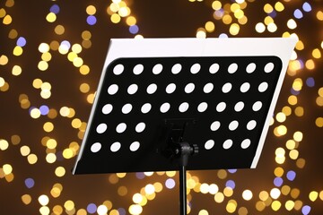Note stand with music sheets against blurred lights, closeup. Bokeh effect