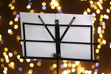 Note stand with music sheets against blurred lights, closeup. Bokeh effect