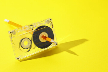 Rewinding audio cassette with pencil on yellow background, closeup. Space for text