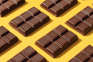 Fototapeta premium delicious chocolate bars neatly arranged on bright yellow surface, top-down view, rich tones