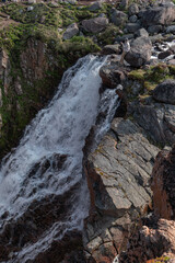 Woman standing on rocks near the powerful Battery waterfall, capturing the scene with her smartphone against rugged Arctic nature