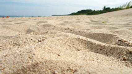 A close up view of textured beach sand with subtle undulations and small pebbles, extending towards a blurred coastline under a bright sky. Perfect for natural, travel, or summer themes.