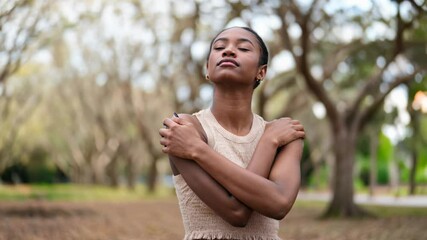 Young black woman embracing herself with a peaceful, introspective expression connecting with nature.