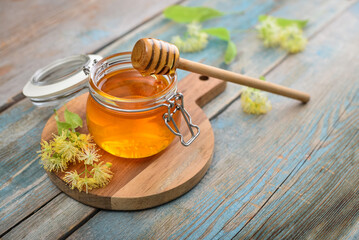 Linden honey in glass jar with wooden honey dipper