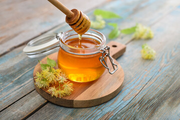 Linden honey in glass jar with wooden honey dipper