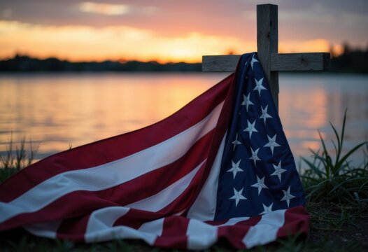 American flag draped over a wooden cross near a lakeside at sunset - Powered by Adobe