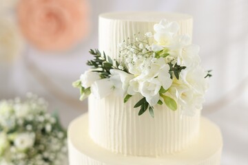 Delicious wedding cake with floral decor and bouquet on table indoors, closeup