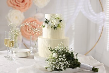 Delicious wedding cake with floral decor, bouquet and glasses of champagne on table indoors