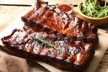 Tasty roasted pork ribs served with rosemary, sauce and salad on wooden table, closeup