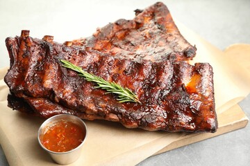 Tasty roasted pork ribs served with rosemary and sauce on light grey table, closeup