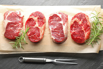Pieces of raw beef meat, spices and carving fork on black table, flat lay