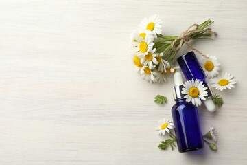 Bottles of essential oil and chamomile flowers on light wooden table, flat lay. Space for text