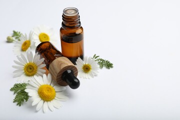 Bottles of essential oil and chamomile flowers on white background, closeup. Space for text