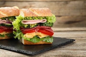 Tasty baguette sandwich with ham and vegetables on wooden table, closeup. Space for text