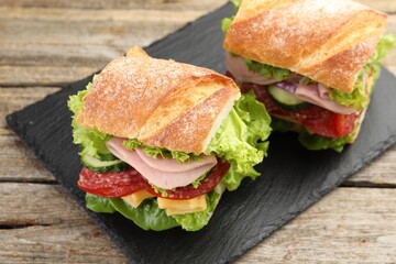 Tasty baguette sandwich with ham and vegetables on wooden table, closeup