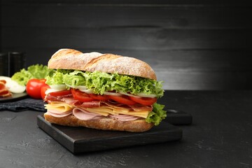 Tasty baguette sandwich with ham and vegetables on black table, closeup. Space for text