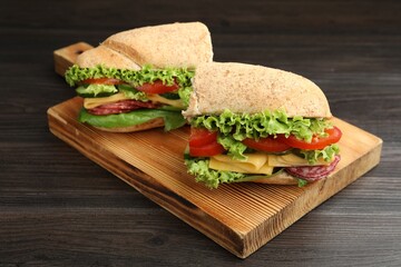 Pieces of tasty baguette sandwich with smoked sausage, cheese and vegetables on wooden table, closeup
